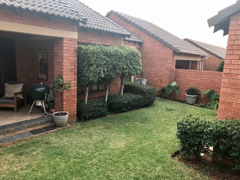 A private rear garden featuring a covered patio with tiled flooring, established landscaping, and brick boundary walls, providing a pleasant outdoor living space.