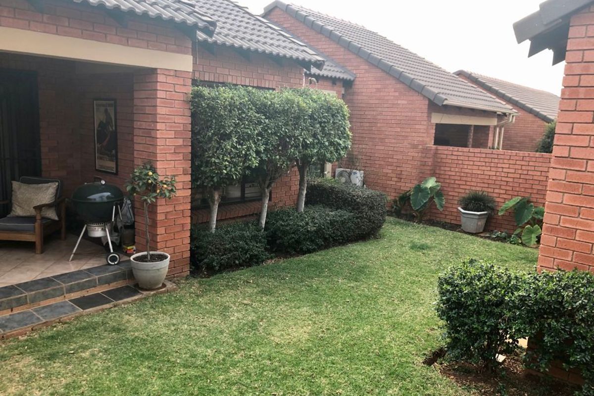 A private rear garden featuring a covered patio with tiled flooring, established landscaping, and brick boundary walls, providing a pleasant outdoor living space.