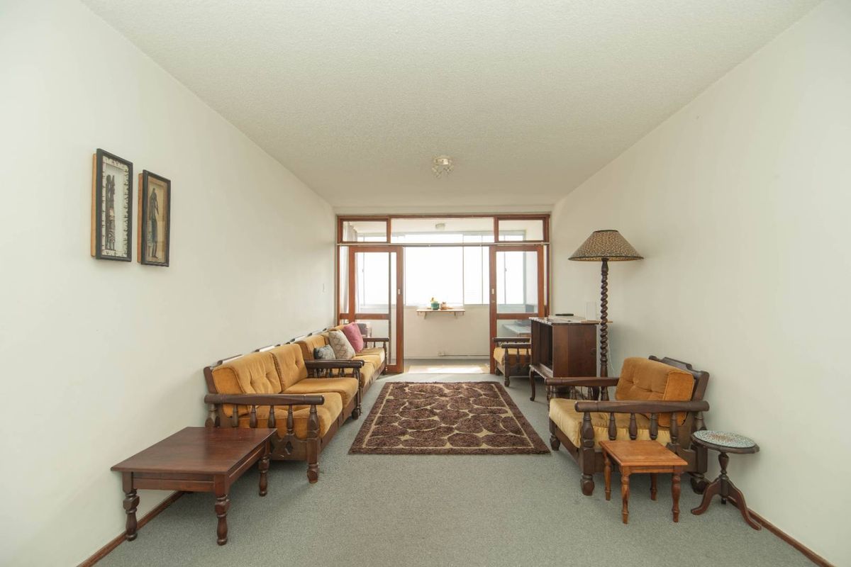 A spacious living room featuring carpeted flooring and large sliding glass doors that provide access to an enclosed balcony area.