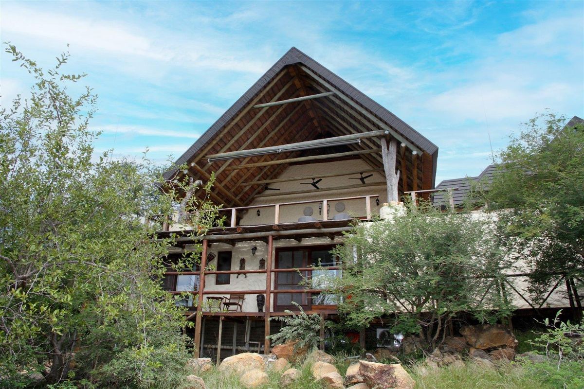 A rustic exterior view of a multi-level house featuring a steep thatched roof, timber balcony railings, and natural stone landscaping.
