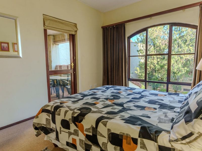 A bedroom featuring an arched window with garden views and a glass door providing direct access to a private balcony.