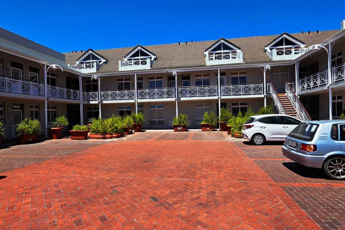 A well-maintained office complex courtyard featuring brick paving, multi-level balconies with wrought iron railings, and dormer windows under a tiled roof.
