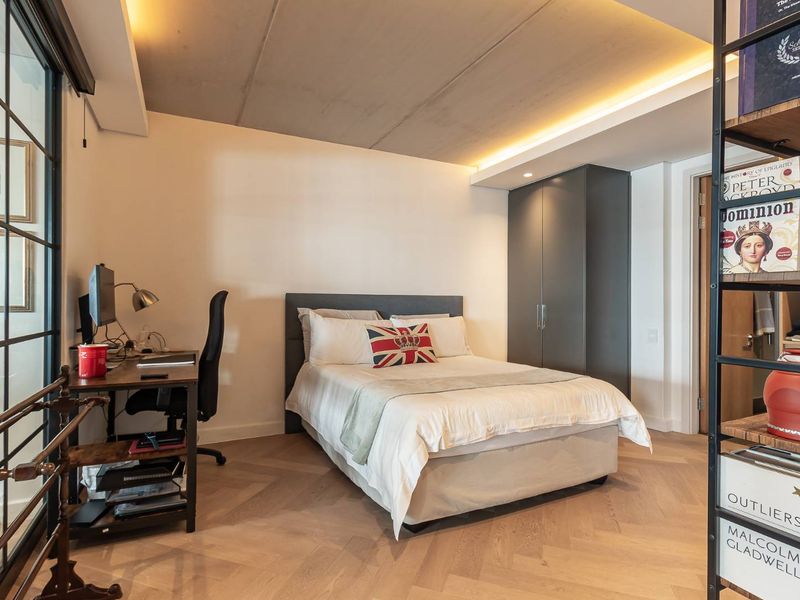 Modern bedroom featuring herringbone timber flooring, exposed concrete ceiling with integrated cove lighting, and built-in dark grey cabinetry.