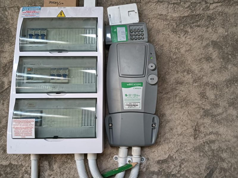 Wall-mounted electrical distribution board and prepaid electricity meter with protective conduit housing.