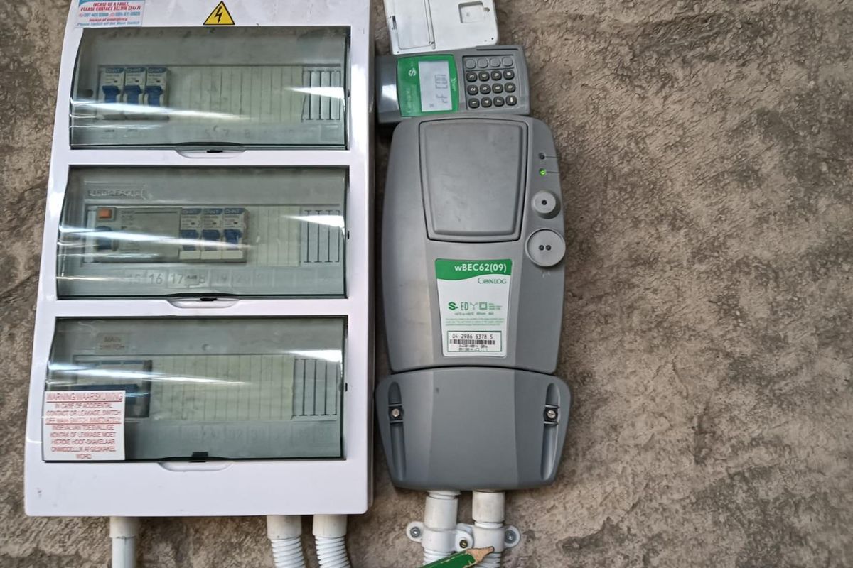 Wall-mounted electrical distribution board and prepaid electricity meter with protective conduit housing.