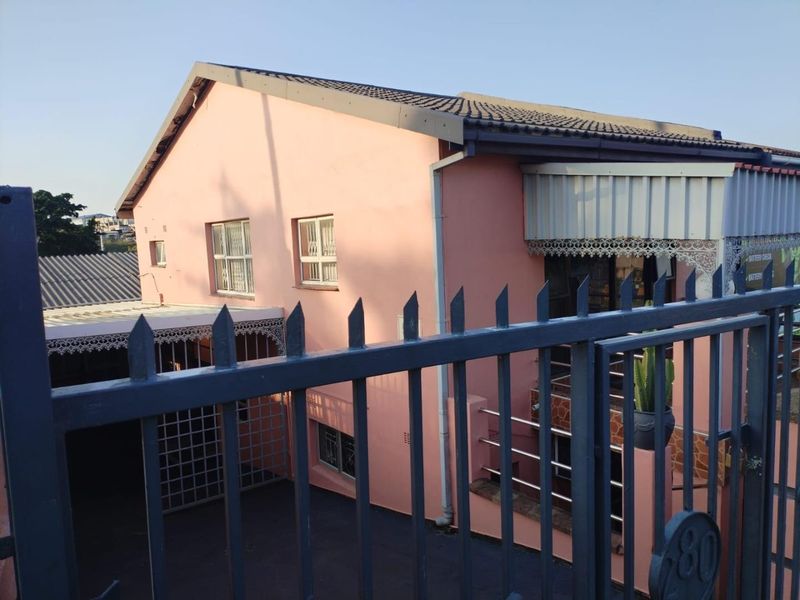 Front view of a residential property featuring pink exterior walls, a tiled roof, and secure metal fencing and security gates.