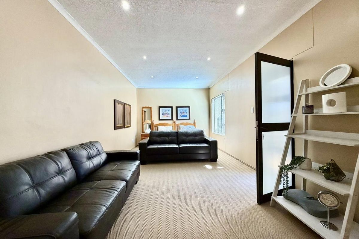 Spacious bedroom featuring recessed ceiling lighting, neutral carpeting, and a glass-panelled door, offering a comfortable and versatile living space.
