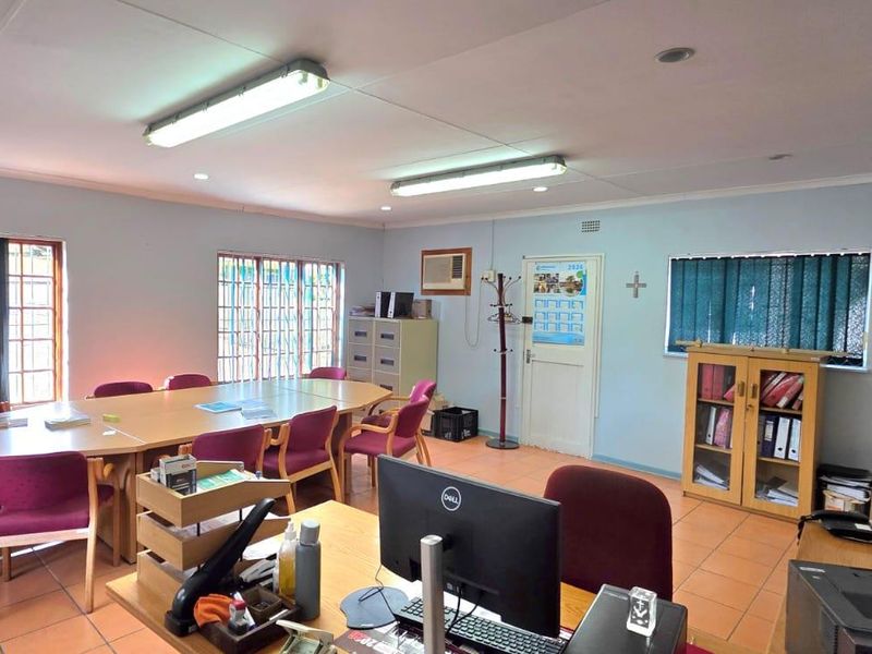 A functional office space featuring tiled flooring, fluorescent lighting, and window security bars, suitable for a professional work environment.