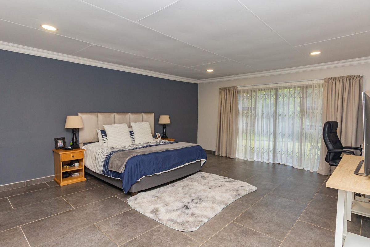Spacious bedroom featuring large format floor tiles, a feature wall, and sliding glass doors with security gate leading to the exterior.