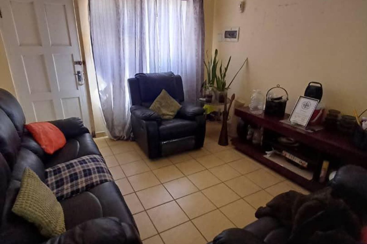 A living room featuring tiled flooring and a standard panel door, currently showing signs of wear on the wall surfaces.