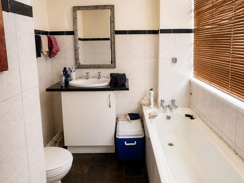 A functional bathroom featuring a vanity unit with basin, a standard bathtub, tiled flooring, and wall tiling with a decorative border.