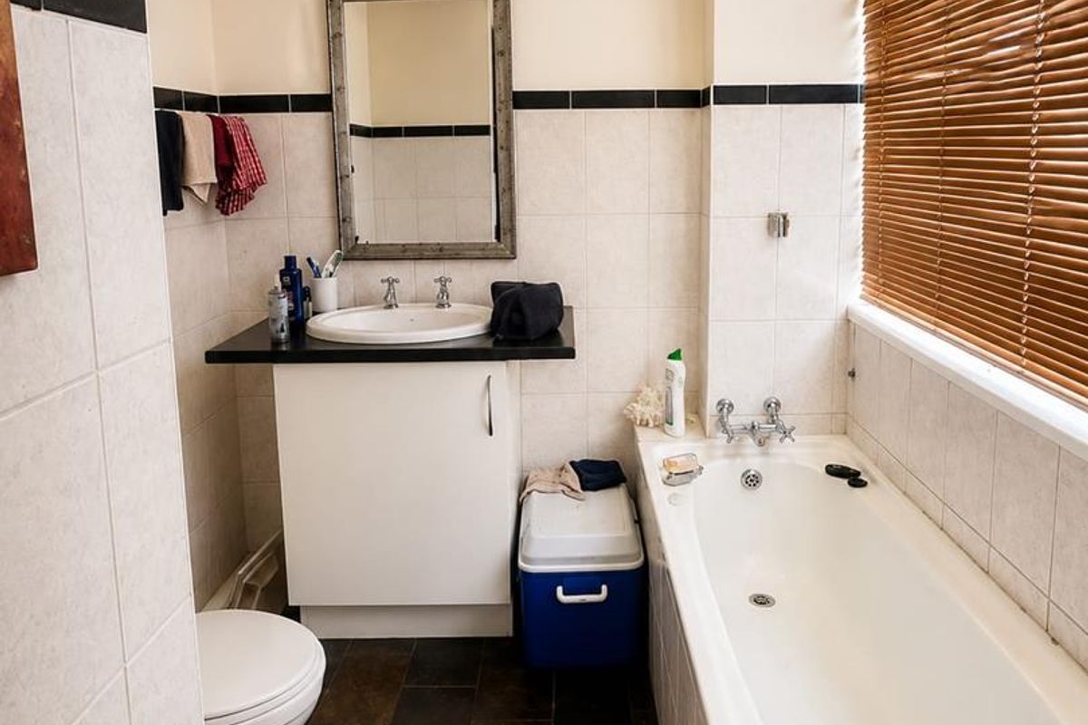 A functional bathroom featuring a vanity unit with basin, a standard bathtub, tiled flooring, and wall tiling with a decorative border.