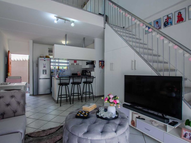 Open-plan living area featuring a kitchen with breakfast bar, tiled flooring, and a staircase leading to an upper level with integrated storage.