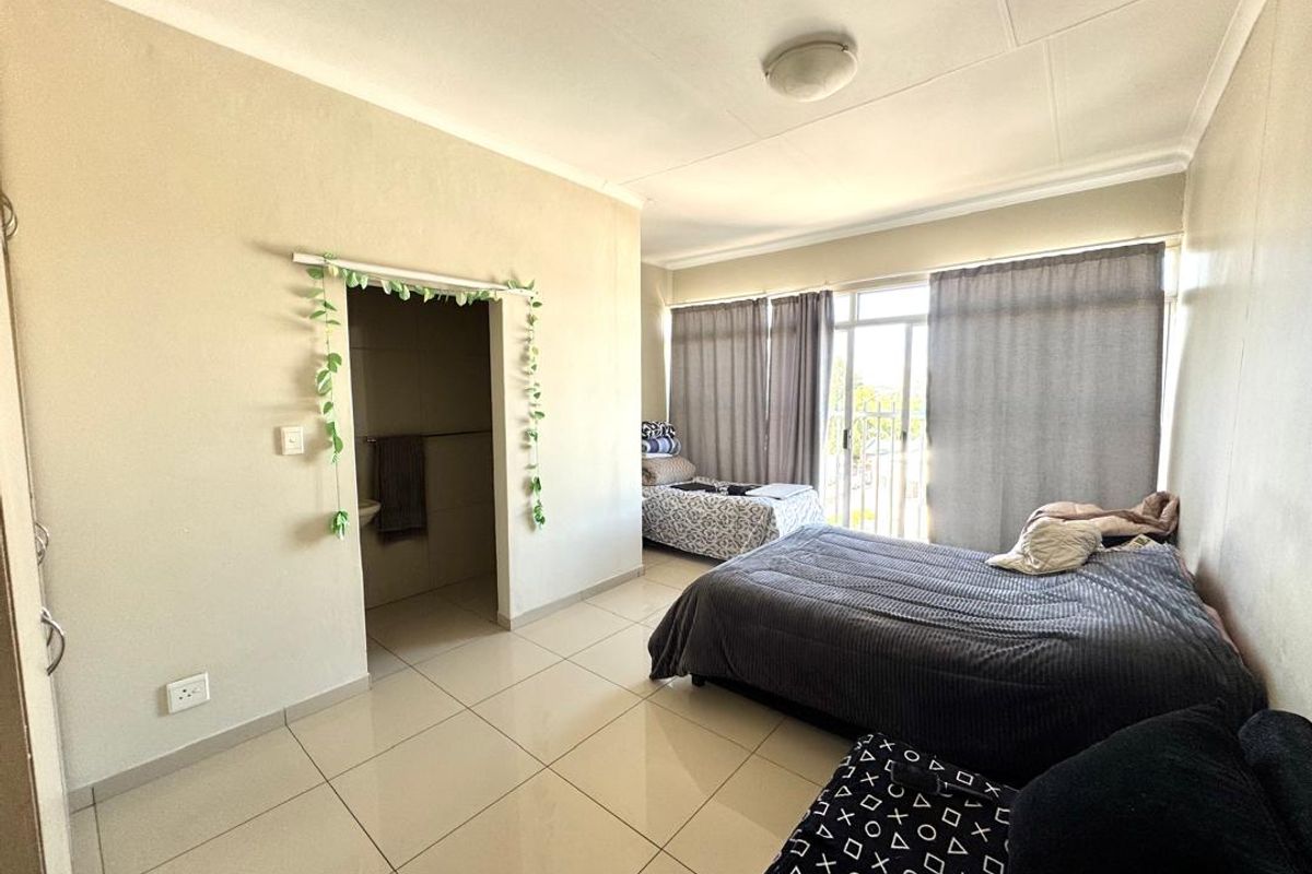 Spacious bedroom featuring tiled flooring, a sliding door leading to a balcony, and direct access to an en-suite bathroom.