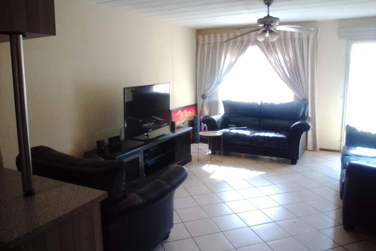 A living room area featuring tiled flooring, a ceiling fan, and a sliding glass door providing natural light.