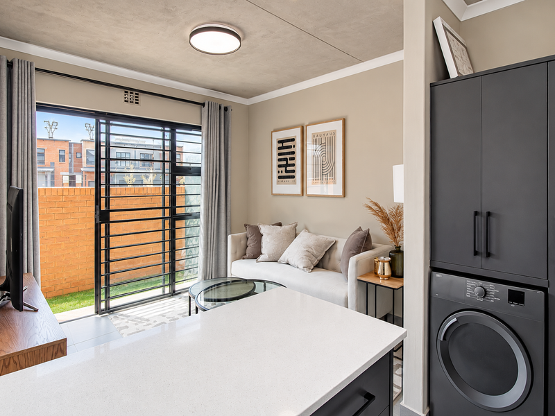 Modern open-plan living area featuring a sleek kitchen island with quartz countertop, integrated laundry appliances, and direct access to a private patio.