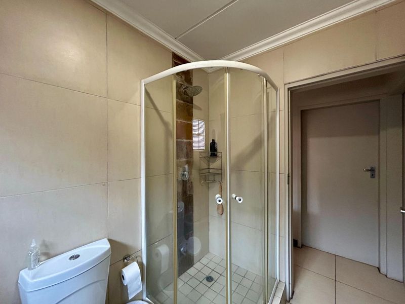 A functional bathroom featuring a corner shower enclosure, tiled walls, and standard toilet fixtures.