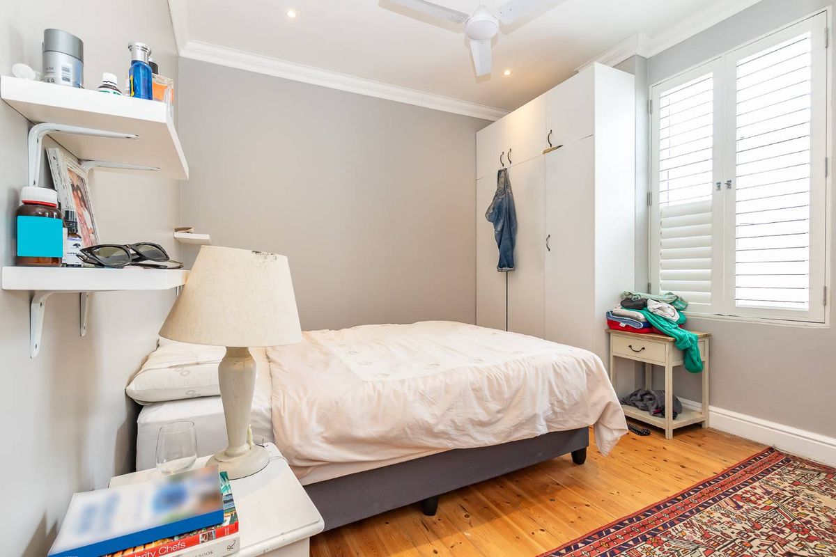 A well-maintained bedroom featuring polished timber flooring, built-in white cabinetry, and plantation shutters, offering a bright and functional living space.