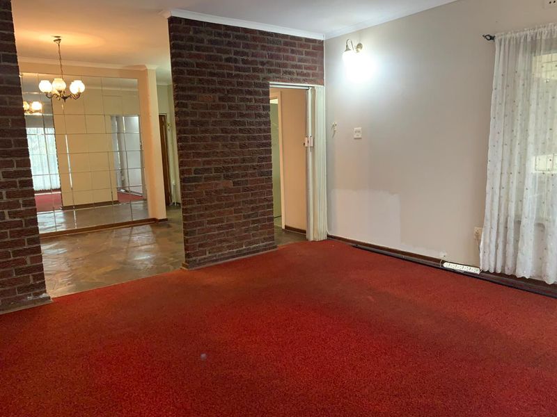Spacious living area featuring an exposed brick accent wall, mirrored wall panels, and carpet flooring, offering a blank canvas for renovation.