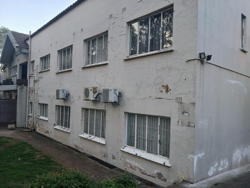 Exterior view of an apartment building facade showing significant plaster cracking, peeling paint, and multiple mounted air conditioning units.