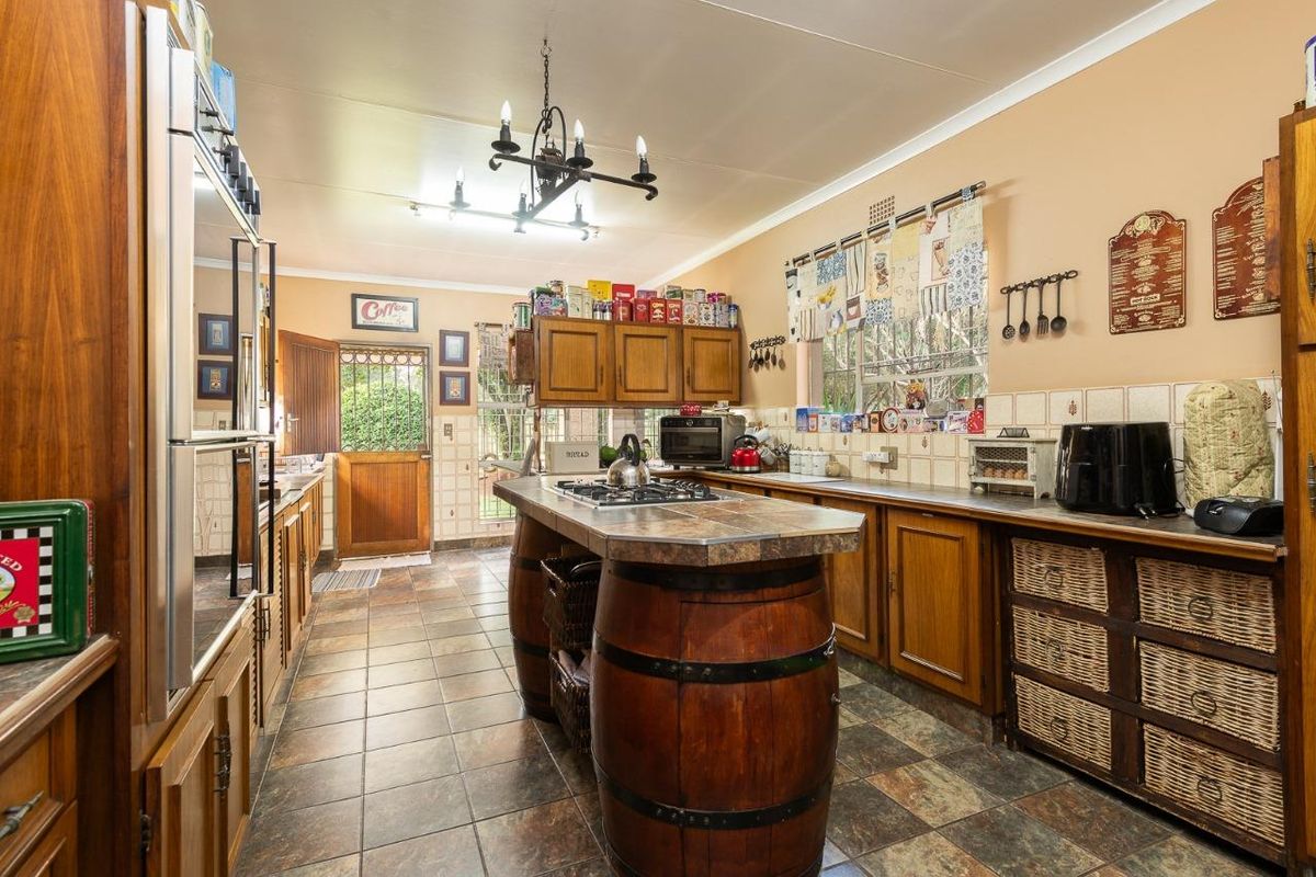 A traditional kitchen featuring wooden cabinetry, a central island with a built-in gas hob, tiled countertops, and direct access to the exterior.
