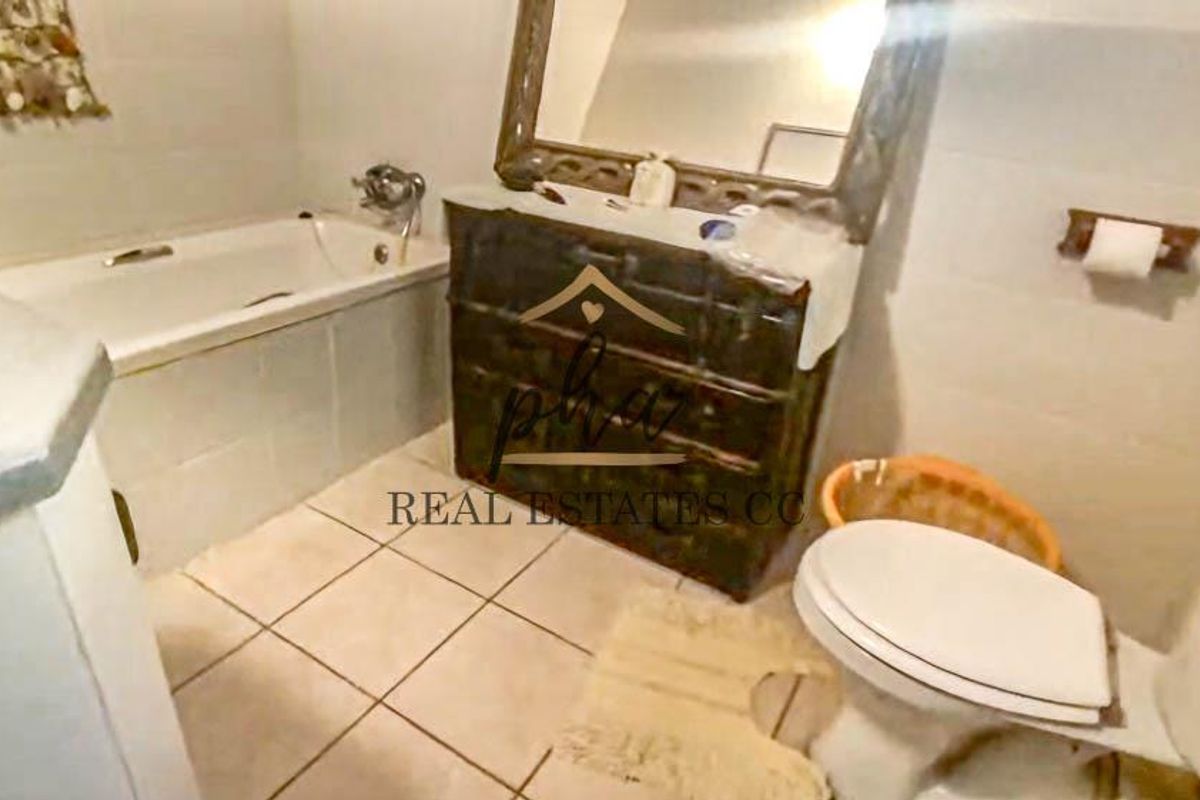 A dated bathroom featuring a built-in bathtub, vanity cabinet, and standard toilet, requiring cosmetic updates to modernize the space.