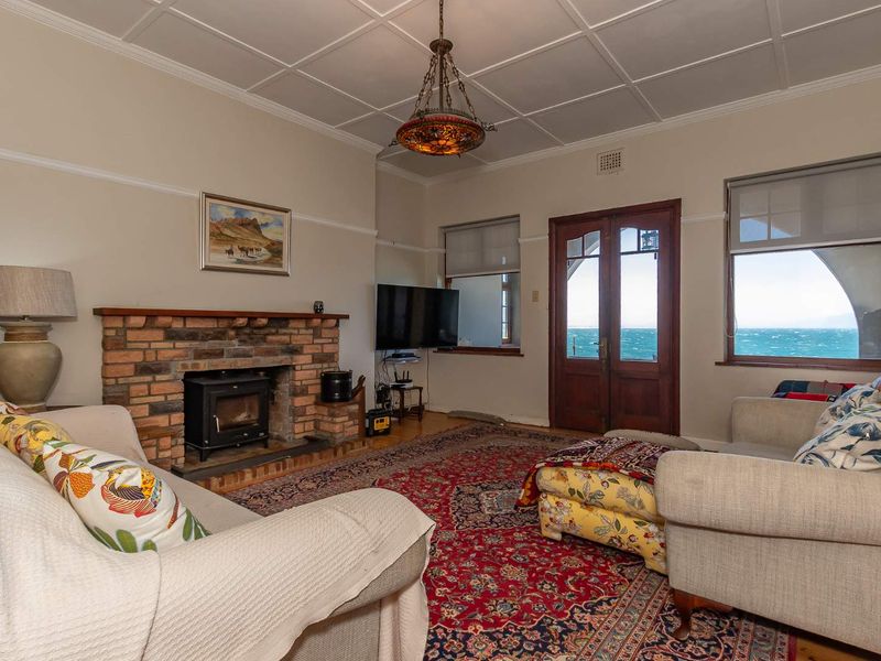 A cozy living room featuring a brick fireplace with a wood-burning stove, timber-framed doors, and expansive ocean views.