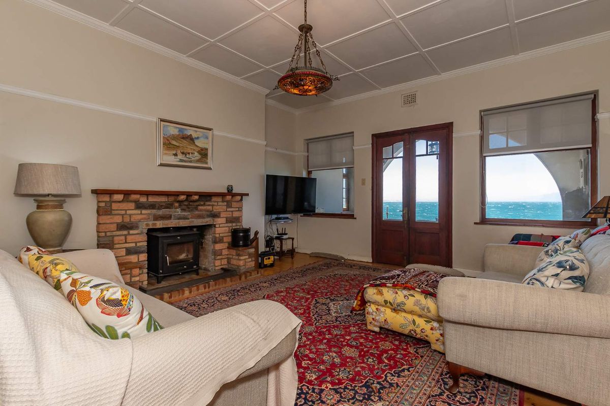 A cozy living room featuring a brick fireplace with a wood-burning stove, timber-framed doors, and expansive ocean views.
