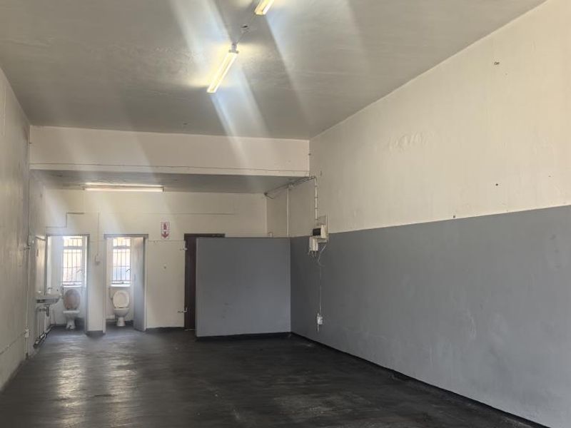 An open-plan utility or commercial space featuring concrete flooring, fluorescent lighting, and two separate toilet cubicles with wash basins.