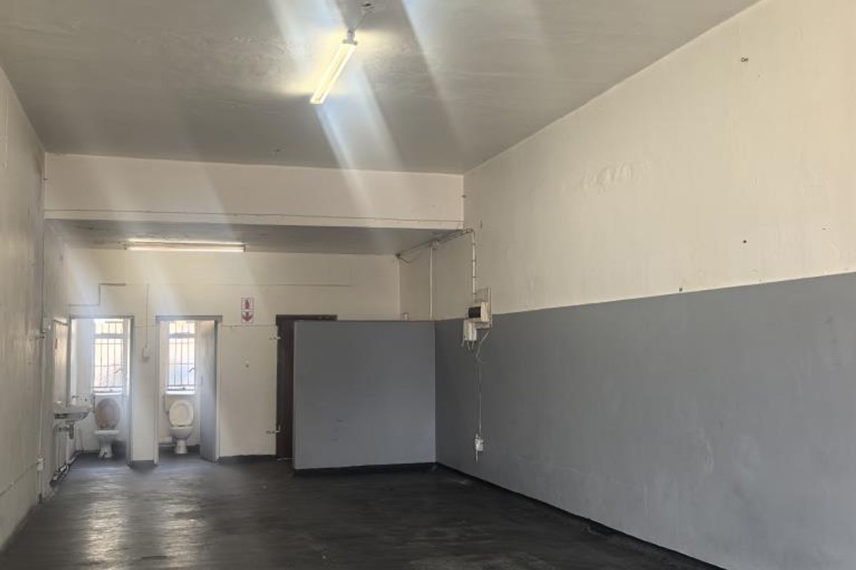 An open-plan utility or commercial space featuring concrete flooring, fluorescent lighting, and two separate toilet cubicles with wash basins.