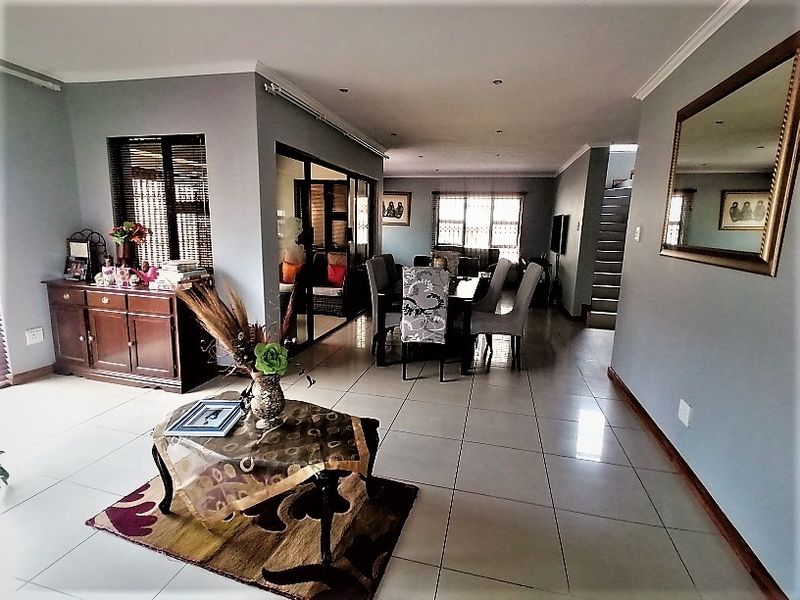 Spacious open-plan living and dining area featuring neutral tiled flooring, recessed lighting, and a staircase leading to the upper level.