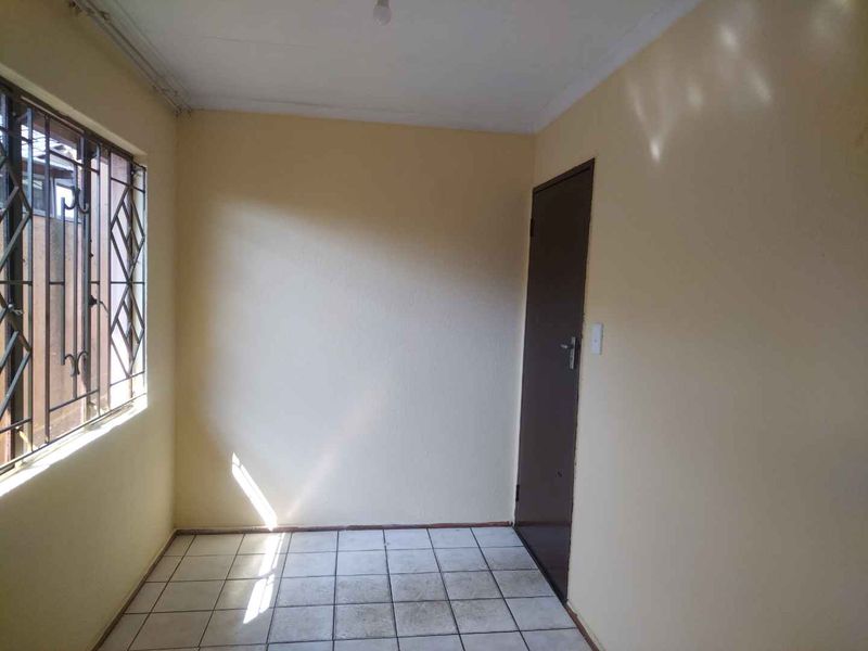 An empty bedroom featuring tiled flooring and a window with security bars, offering a blank canvas for potential interior design updates.