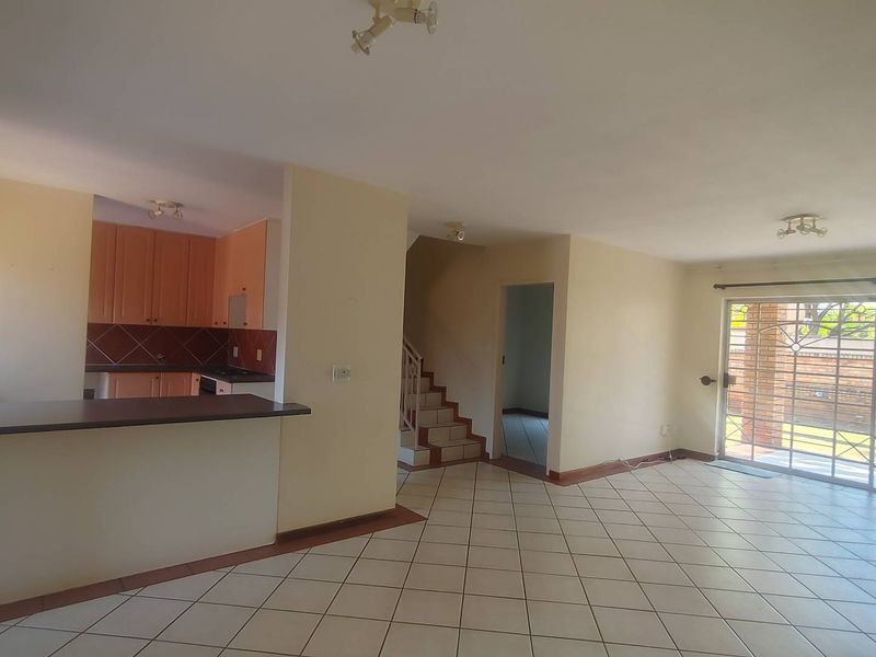 Spacious open-plan living area featuring tiled floors, a functional kitchen with breakfast bar, and direct access to the rear patio through sliding glass doors.