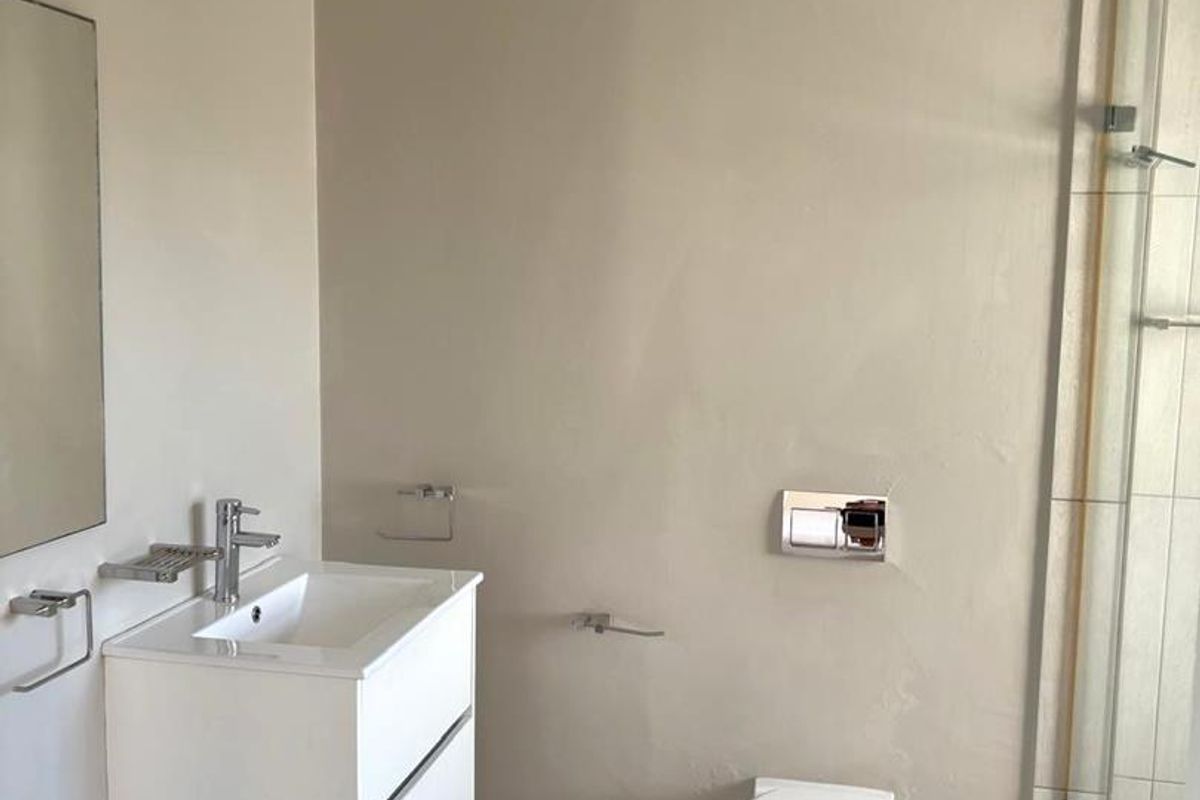 Modern bathroom featuring a wall-mounted vanity, wall-hung toilet with concealed cistern, and a glass-enclosed shower with neutral floor tiling.