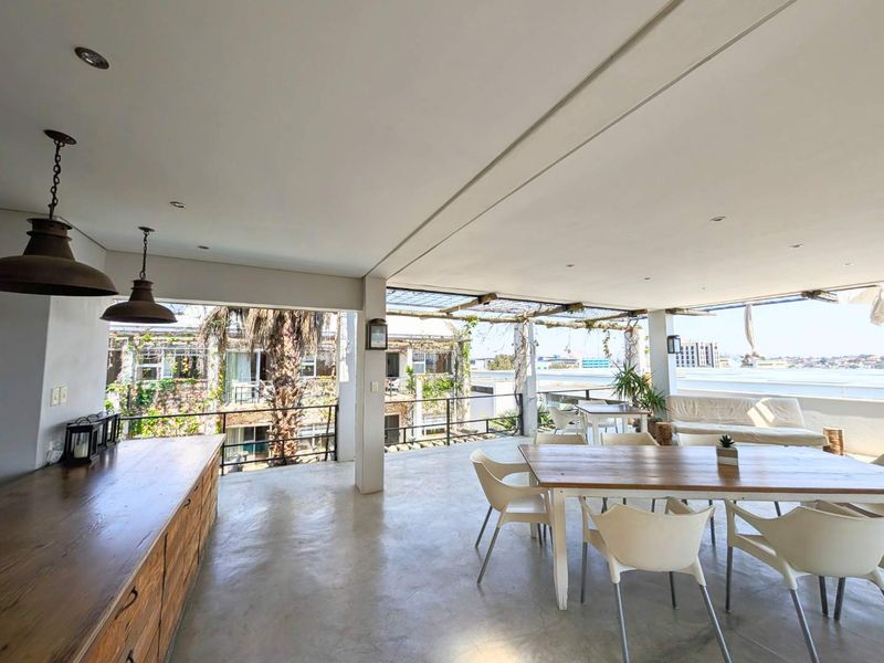 Spacious covered balcony featuring concrete flooring, built-in cabinetry, and an open-air design with metal railings, offering an ideal space for outdoor dining and relaxation.