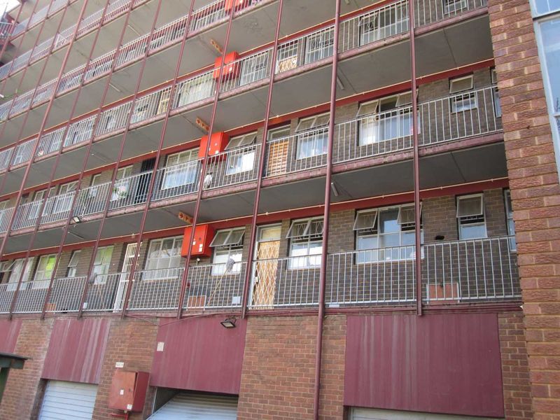 Exterior view of a multi-story apartment building featuring brick facade, metal balcony railings, and security gates on multiple levels.