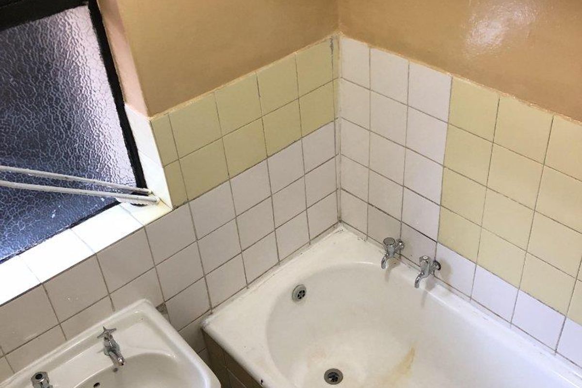 A dated bathroom featuring a standard bathtub, basin, and tiled splashbacks, requiring cosmetic updates to modernize the space.