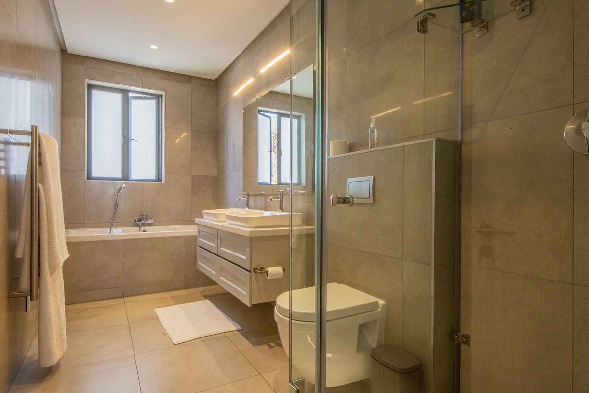 Modern bathroom featuring a double vanity, a built-in bathtub, and a glass-enclosed walk-in shower with neutral floor-to-ceiling tiling.