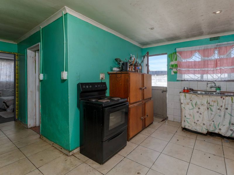 A dated kitchen featuring a freestanding stove, double basin sink, and tiled flooring, requiring significant cosmetic updates and repairs to the walls and ceiling.