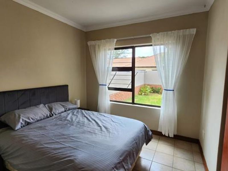 A bedroom featuring tiled flooring, neutral wall tones, and an aluminium-framed window with security bars overlooking the rear garden area.