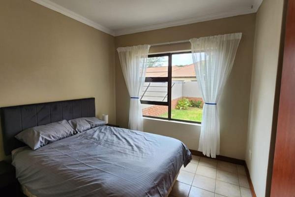 A bedroom featuring tiled flooring, neutral wall tones, and an aluminium-framed window with security bars overlooking the rear garden area.