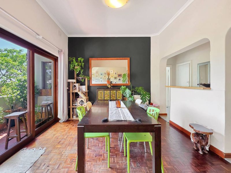 A bright dining room featuring classic parquet flooring, an arched pass-through to the kitchen, and large sliding glass doors leading to an outdoor balcony.