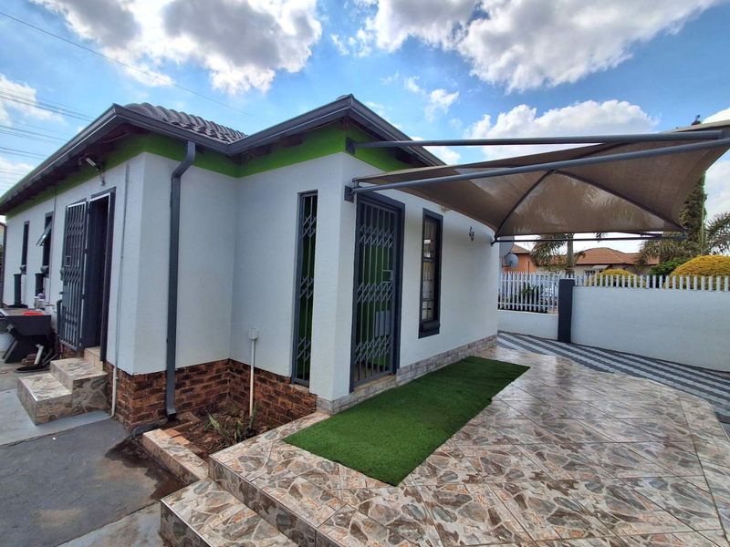 Rear exterior view featuring a tiled patio area with a shade sail, security gates, and a well-maintained facade with brick detailing.