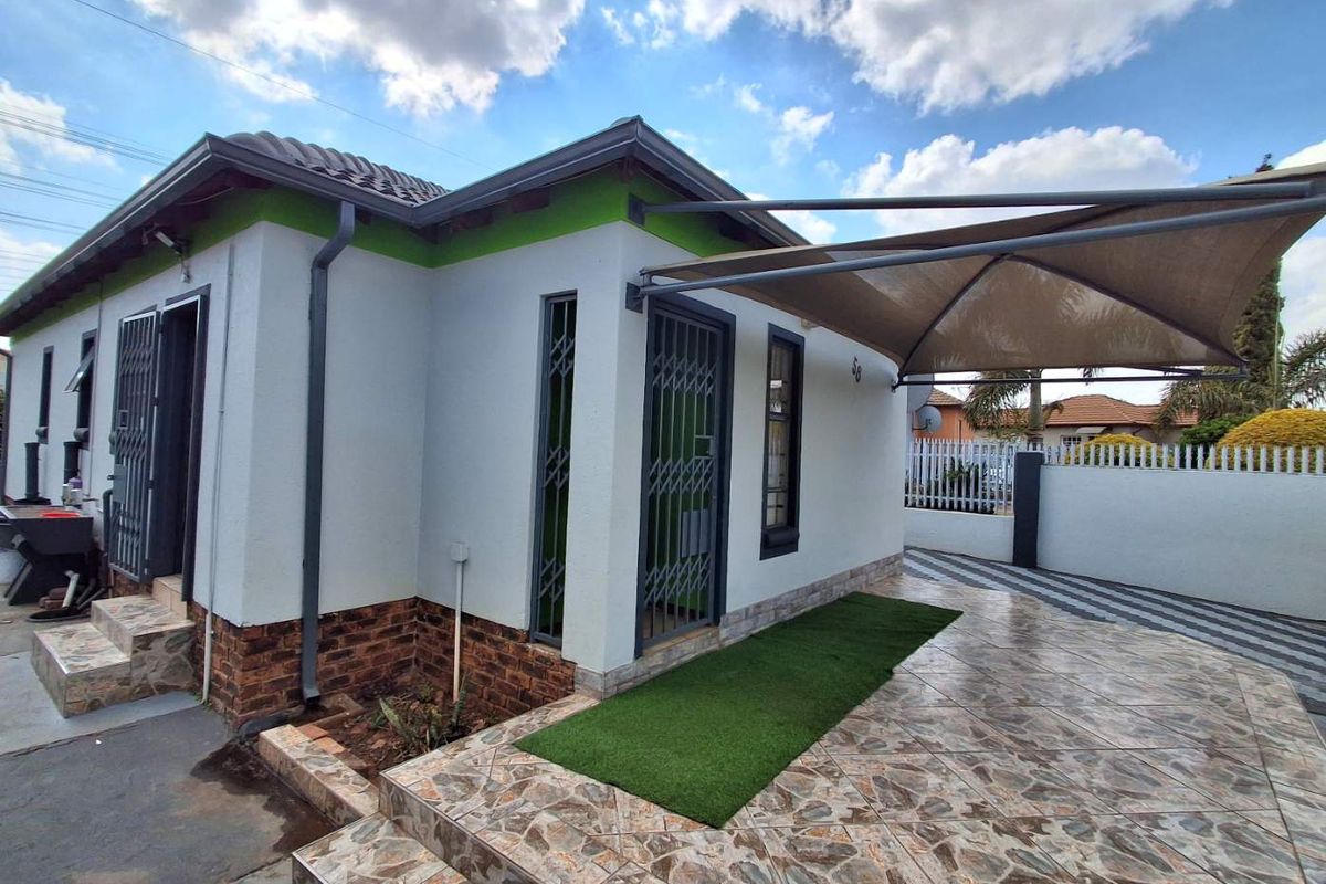 Rear exterior view featuring a tiled patio area with a shade sail, security gates, and a well-maintained facade with brick detailing.