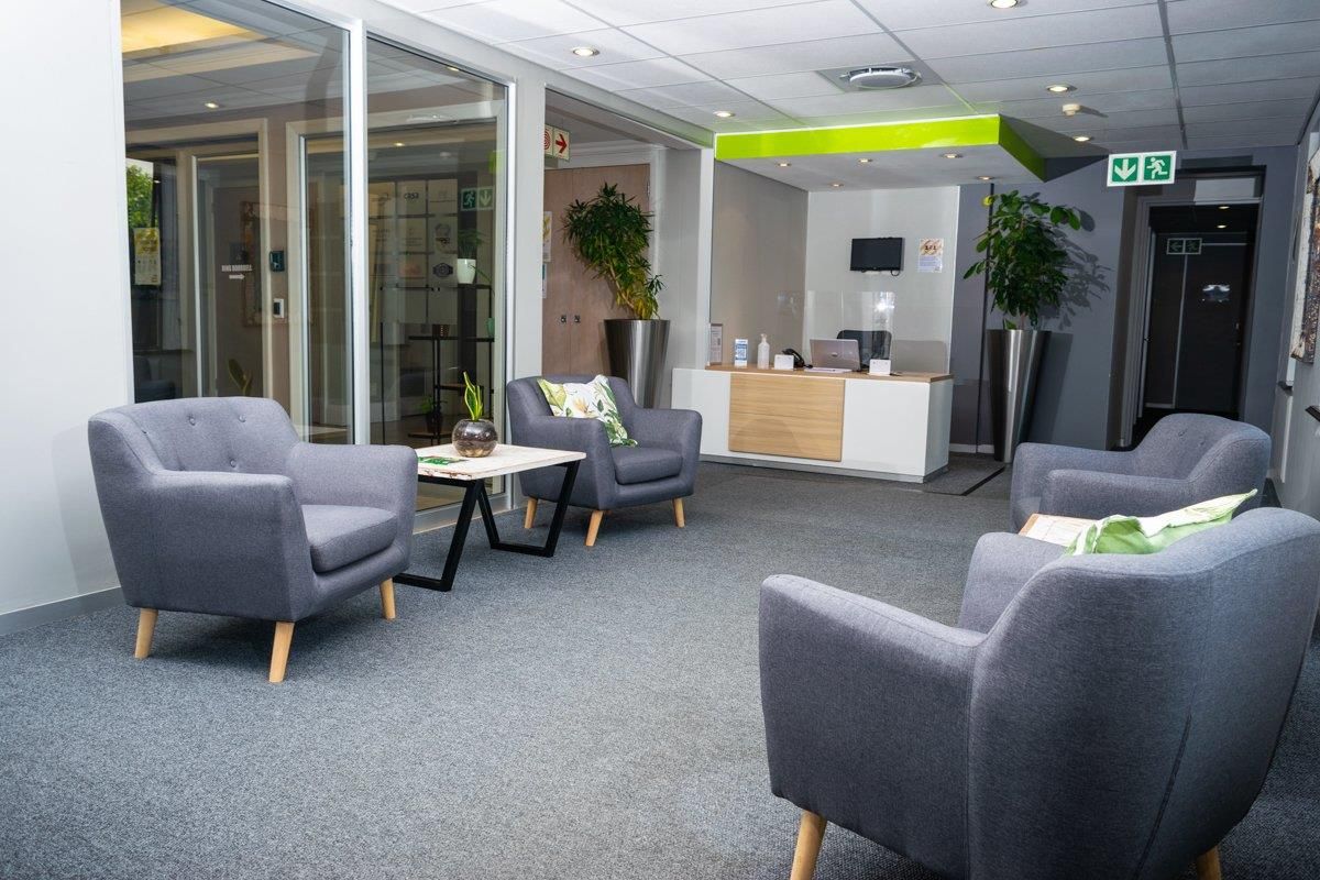 A professional office reception area featuring a modern reception desk, glass-partitioned offices, carpeted flooring, and recessed ceiling lighting.