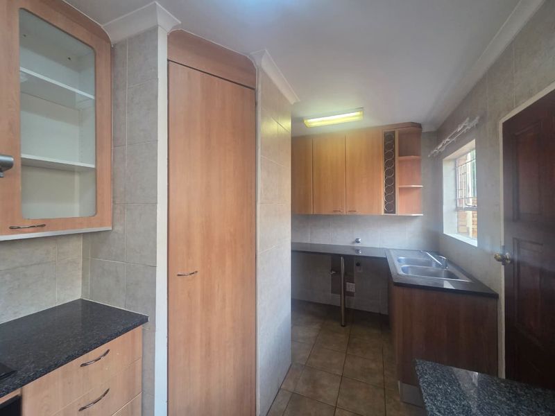 A functional scullery area featuring laminate cabinetry, granite countertops, a double basin sink, and tiled finishes, providing ample space for utility and prep work.