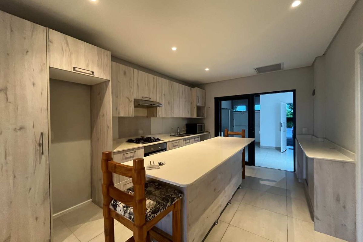 Modern kitchen featuring light wood-grain cabinetry, a central island with stone countertops, integrated gas hob, and tiled flooring with direct access to the exterior.
