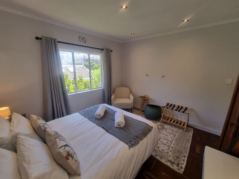 A well-maintained bedroom featuring warm parquet flooring, recessed downlighting, and a large window providing natural light and a pleasant garden view.