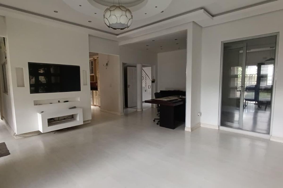 Spacious living area featuring a coffered ceiling with recessed lighting, built-in media console, and large sliding glass doors leading to the exterior.