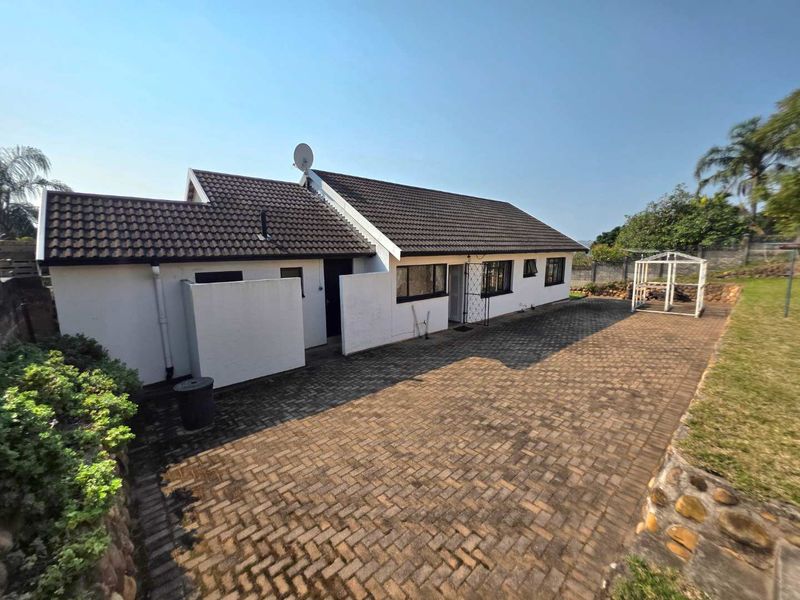 Rear view of the house featuring a tiled roof, paved patio area, and stone retaining wall in the garden.